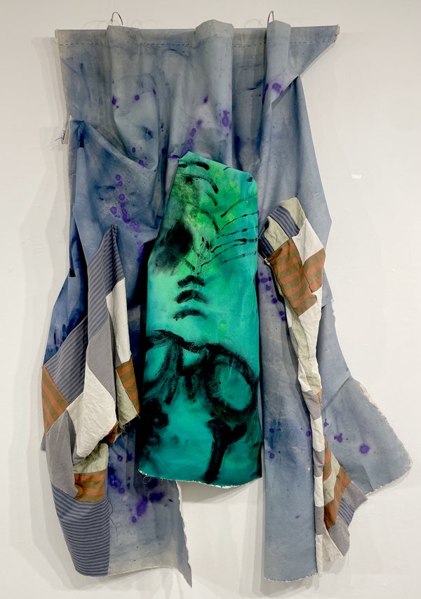 A mixed-fabric wall piece, hung and draped, with a hand-painted green panel at its center.