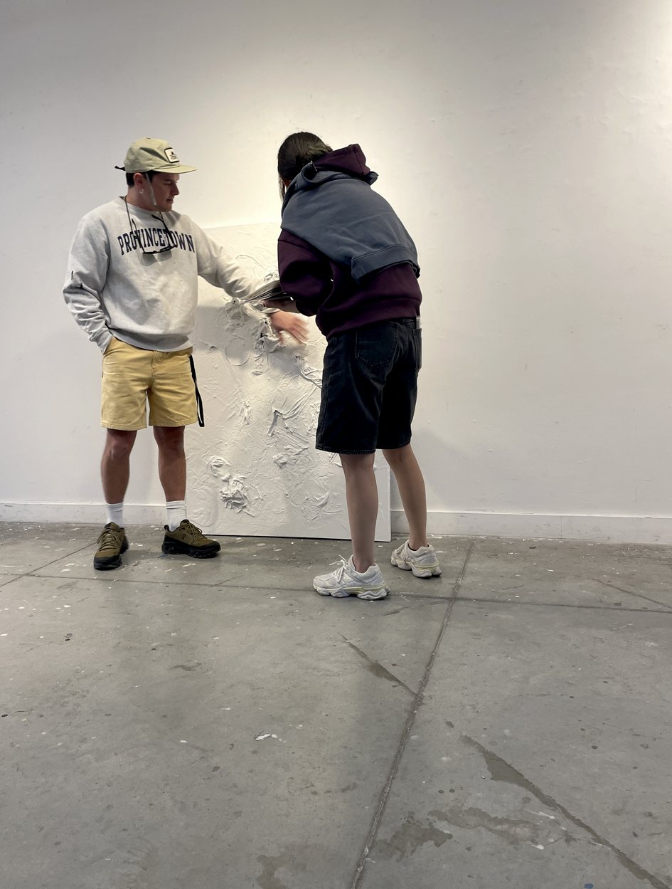 Two students working on a heavily textured white painting in the studio.